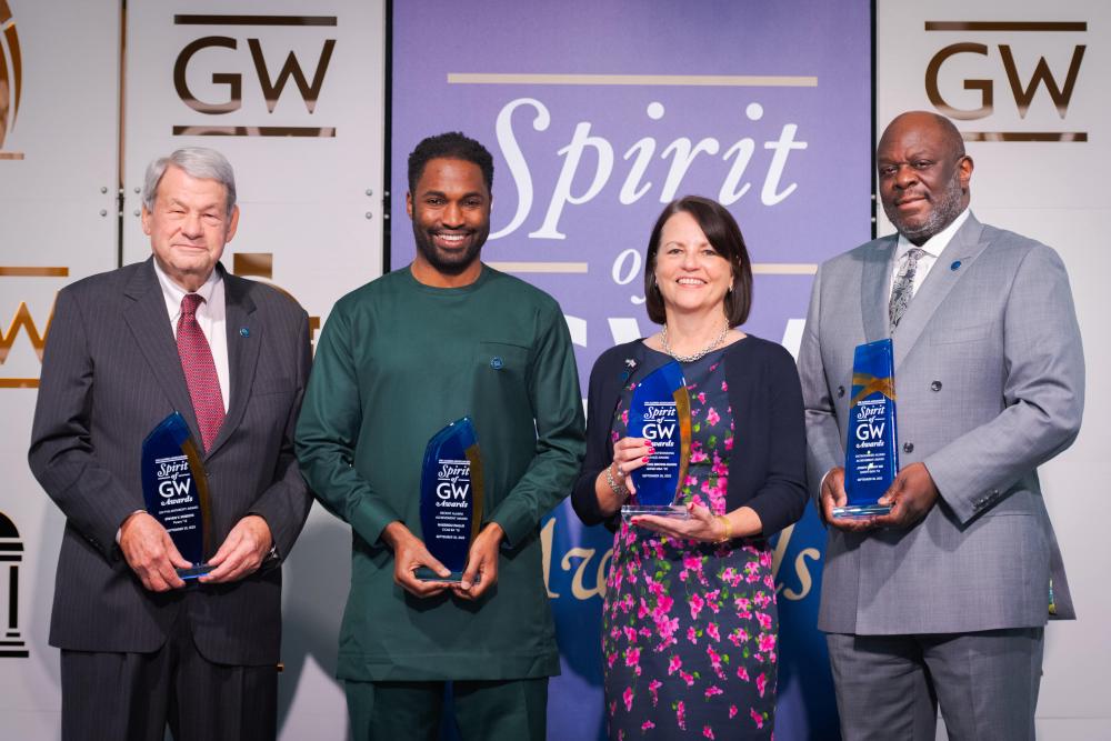 GW Alumni Spirt Awards Four people, holding awards, posing in front of GW banners.